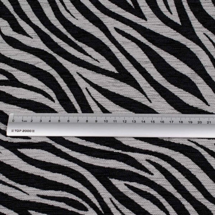 Zebra szaro-czarna. Zbliżenie na materiał tapicerski o grubym splocie, przedstawiający organiczny, zwierzęcy wzór zebry. Kolorystyka to ciemna, nasycona szarość i głęboka czerń, co nadaje tkaninie nowoczesny i drapieżny charakter.