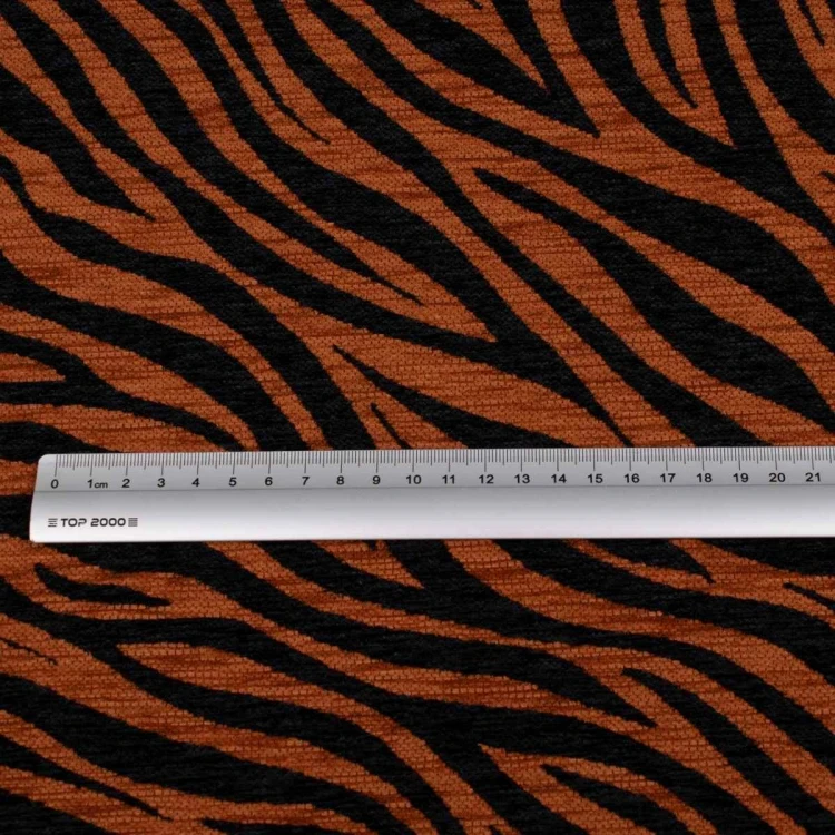 Zebra brązowo-czarna. Fakturowana tkanina tapicerska o gęstym splocie, z wyraźnym, nieregularnym wzorem pasów zebry w ciepłym odcieniu brązu i kontrastującej czerni. Zdjęcie z miarą